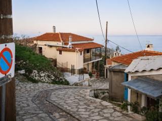 Σοκάκι με πέτρινα σπίτια στους Κοσμαδαίους Σάμου με φόντο τη θάλασσα.